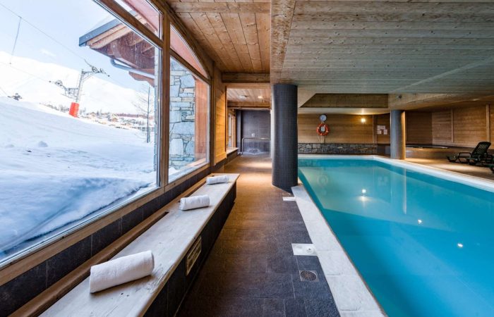 Basen z panoramicznym widokiem na ośnieżone stoki – połączenie relaksu i alpejskiego krajobrazu. Drewniane wykończenia i ciepłe światło tworzą idealną atmosferę do odpoczynku po dniu na nartach